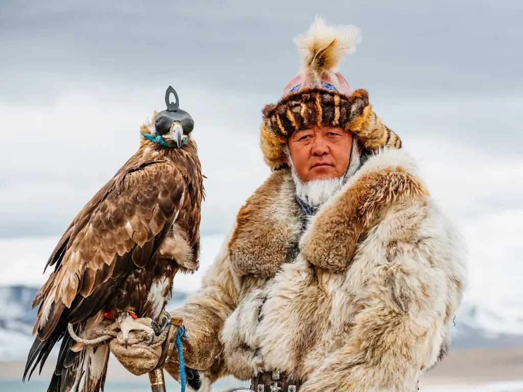 An eagle hunter in a fox-fur coat holding his golden eagle