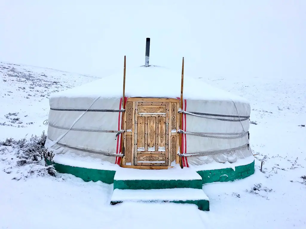 A ger with a carved wooden door in fresh snow
